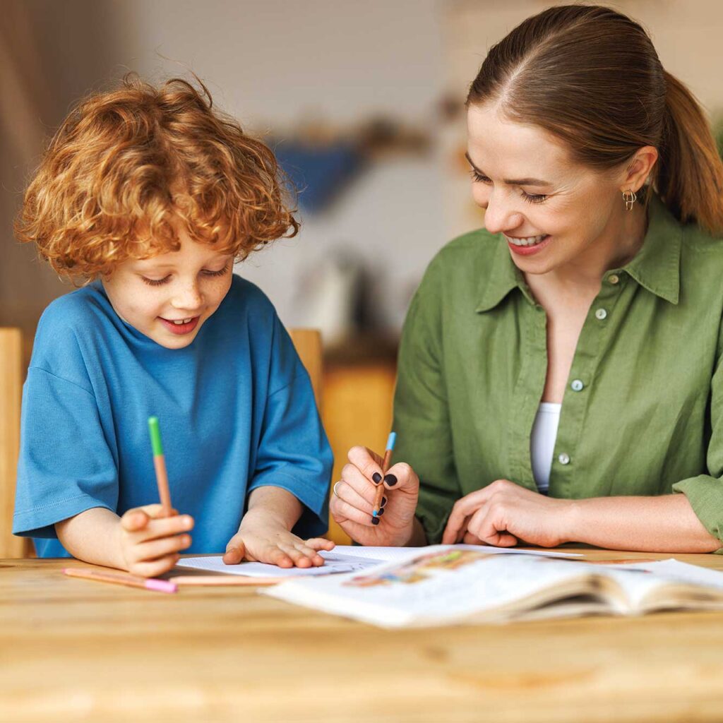 a woman sits holding a pencil with a young boy holding a pencil while working through a workbook