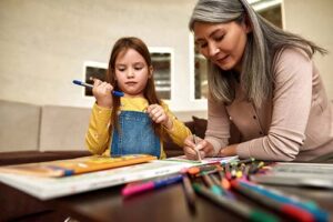 a woman colors in a coloring book with a young girl and thinks about how important parent and caregiver education is to a child's well being