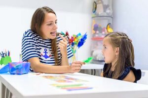 a specialist points at her mouth and is working with a young girl in early intensive behavioral intervention
