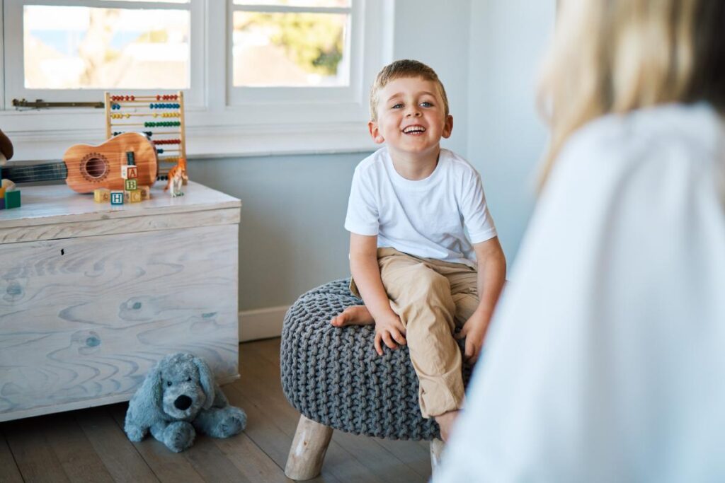 a young boy sits on a stool learning verbal behavior techniques with his behavior specialist
