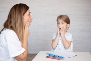 an aba specialist sits at a table with a young girl and works with her in verbal behavior therapy in gaithersburg