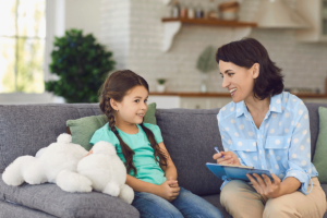 an adult woman aba specialist sits on a couch with a young girl developing her behavior intervention plan