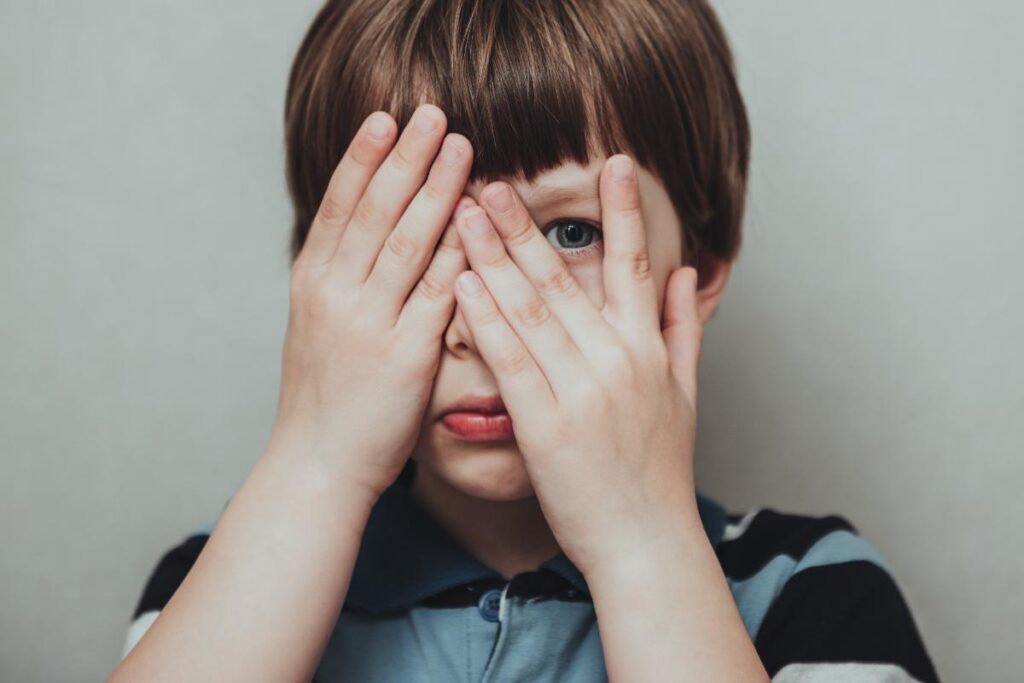 a child with profound autism covers his face with his hands and peeking out between his fingers