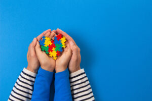 a child holds puzzle pieces in shape of a heart while adult holds the childs hands while discussing autism stereotypes