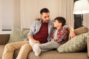 a man sits on a couch with his young son wondering to himself how to communicate with a nonverbal autistic child