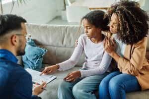 a mother sits with her daughter on a couch and with a specialist during her daughters autism therapy at home