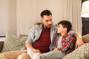 a man sits with his son on a couch and wonders about tips on autism spectrum communication strategies