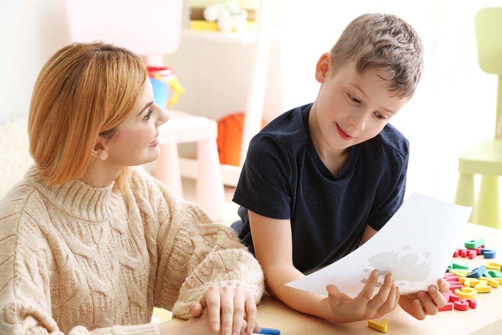 a woman works with a child who is looking at a piece of paper and asking woman what is extinction in aba